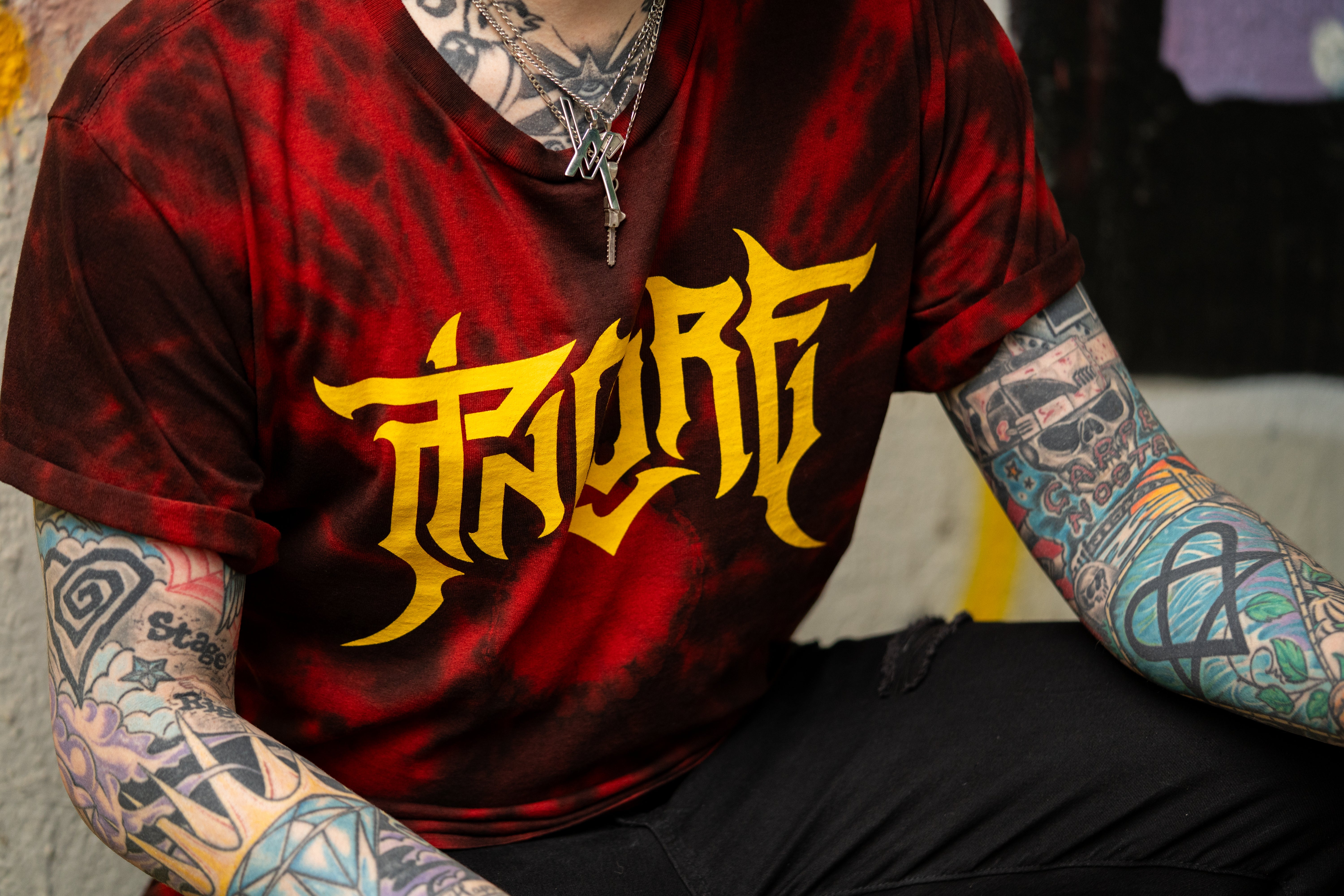 Image of Red tie dye T shirt with bold yellow gothic logo worn by tattooed model Pincore Merchandise streetwear