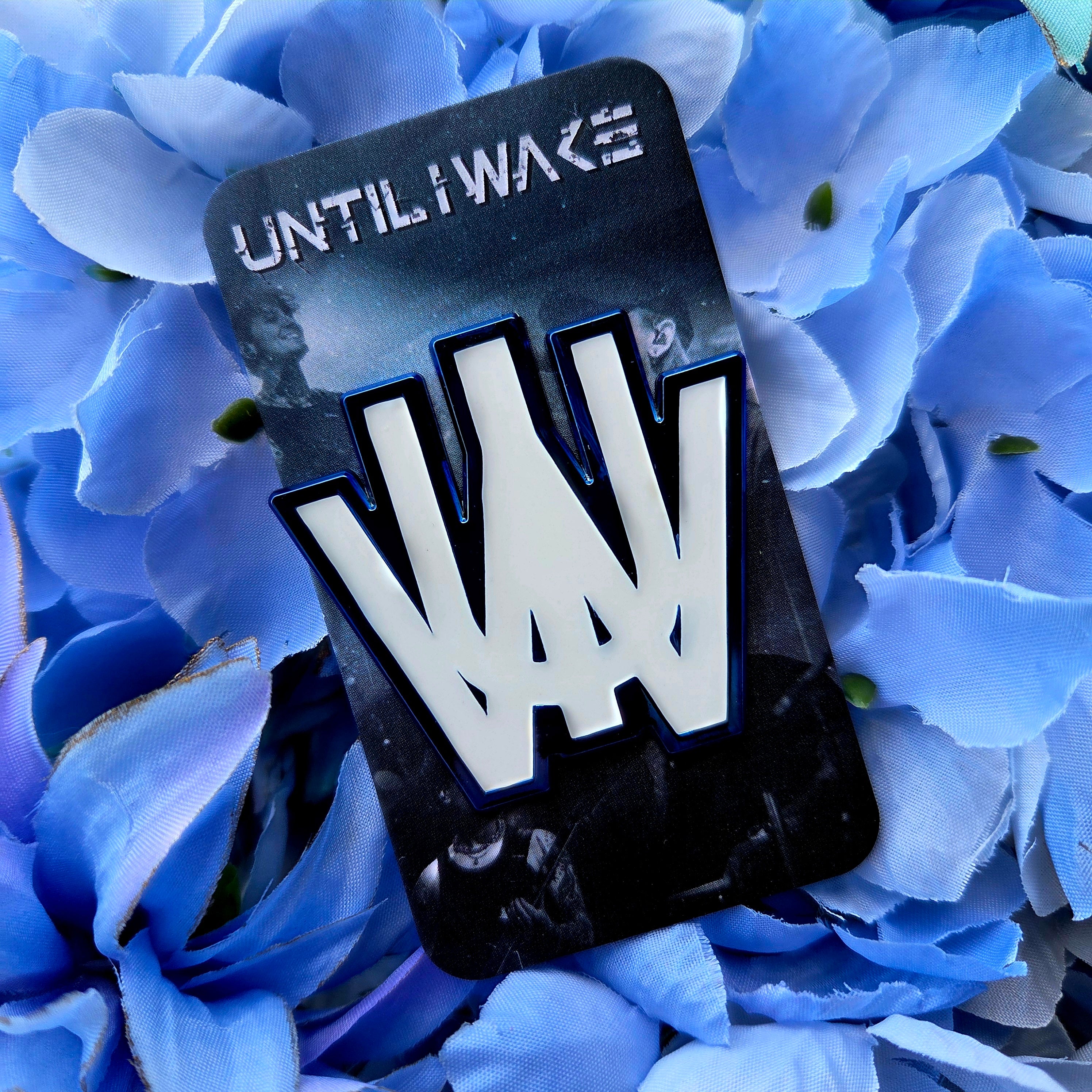 Until I Wake enamel pin by Pincore Merchandise white logo enamel pin on black card backing over blue flowers