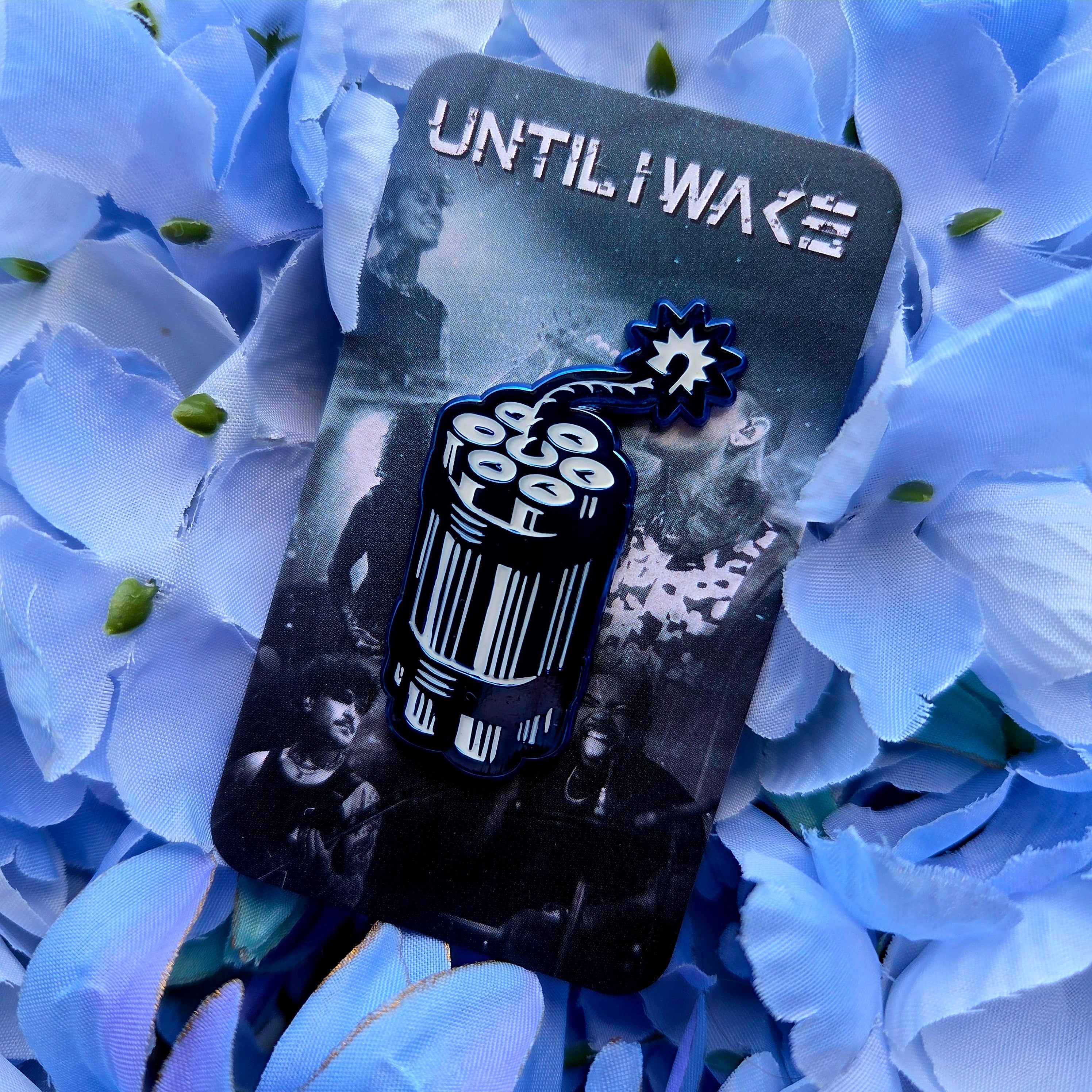 Image of Until I Wake enamel pin black and white dynamite design on band backing card by Pincore Merchandise surrounded by blue flowers