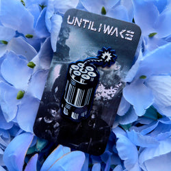 Image of Until I Wake enamel pin black and white dynamite design on band backing card by Pincore Merchandise surrounded by blue flowers