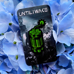 Image of Until I Wake enamel pin green dynamite design on band photo backing card on blue floral background
